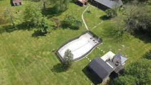 Eine Vogelperspektive eines Wohngebiets mit großzügiger Freifläche, einem eingezäunten Garten und mehreren Gebäuden, darunter ein Haus mit Satteldach und ein Schuppen.