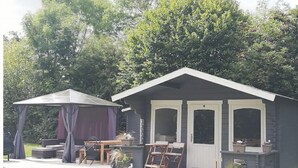 Eine kleine, eingeschossige Holzhütte mit Veranda, überdachter Sitzgelegenheit und einer Terrasse.