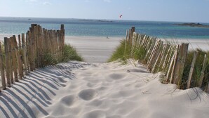 Une plage de sable bordée d’une clôture en bois, offrant une vue dégagée sur l’océan.