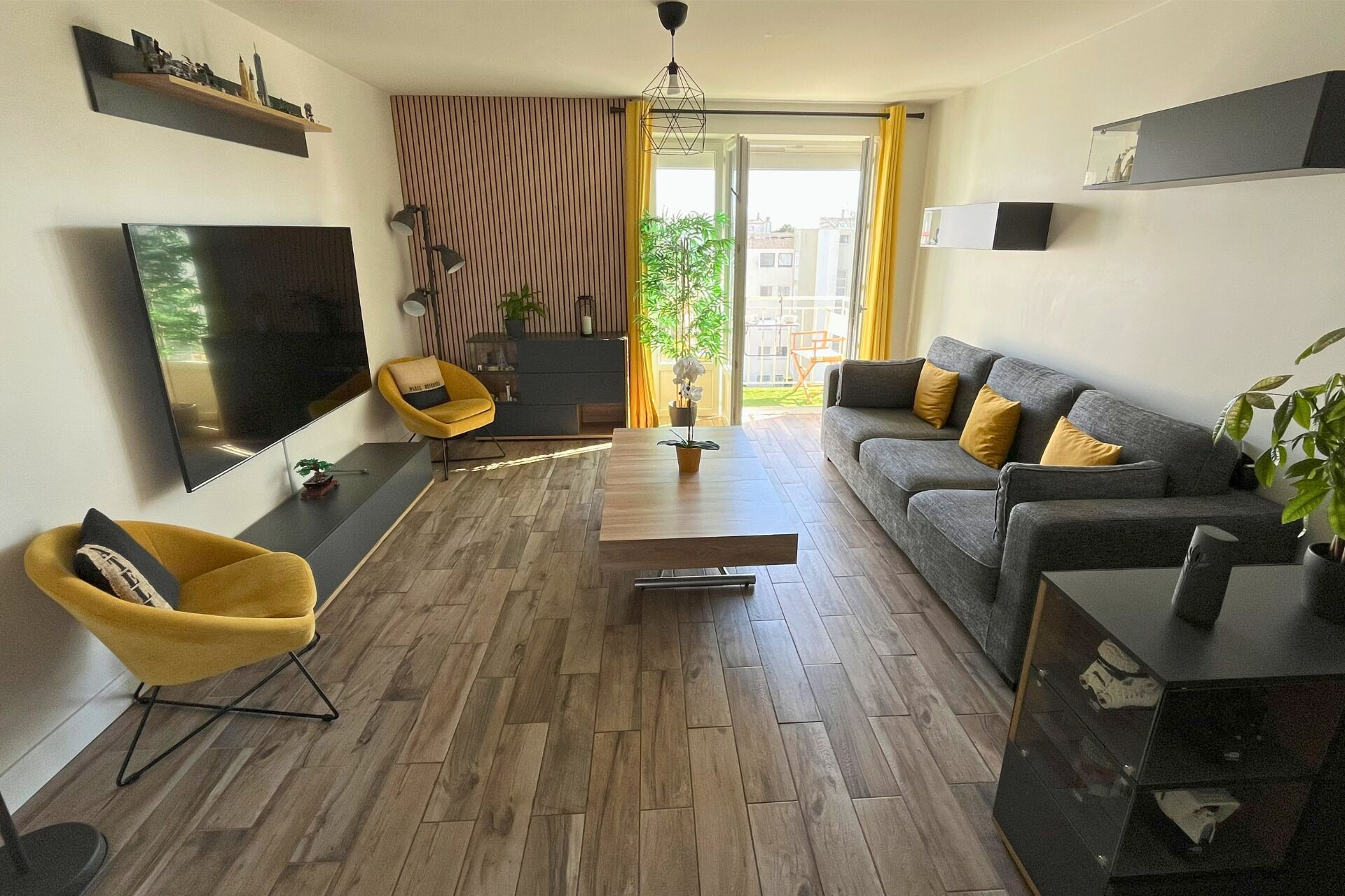 Un salon moderne avec un téléviseur à écran plat, un canapé avec des coussins jaunes, un fauteuil jaune et une table basse en bois.