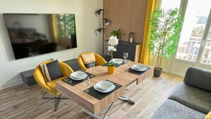 A modern dining area with a wooden table, yellow chairs, and a large TV screen.