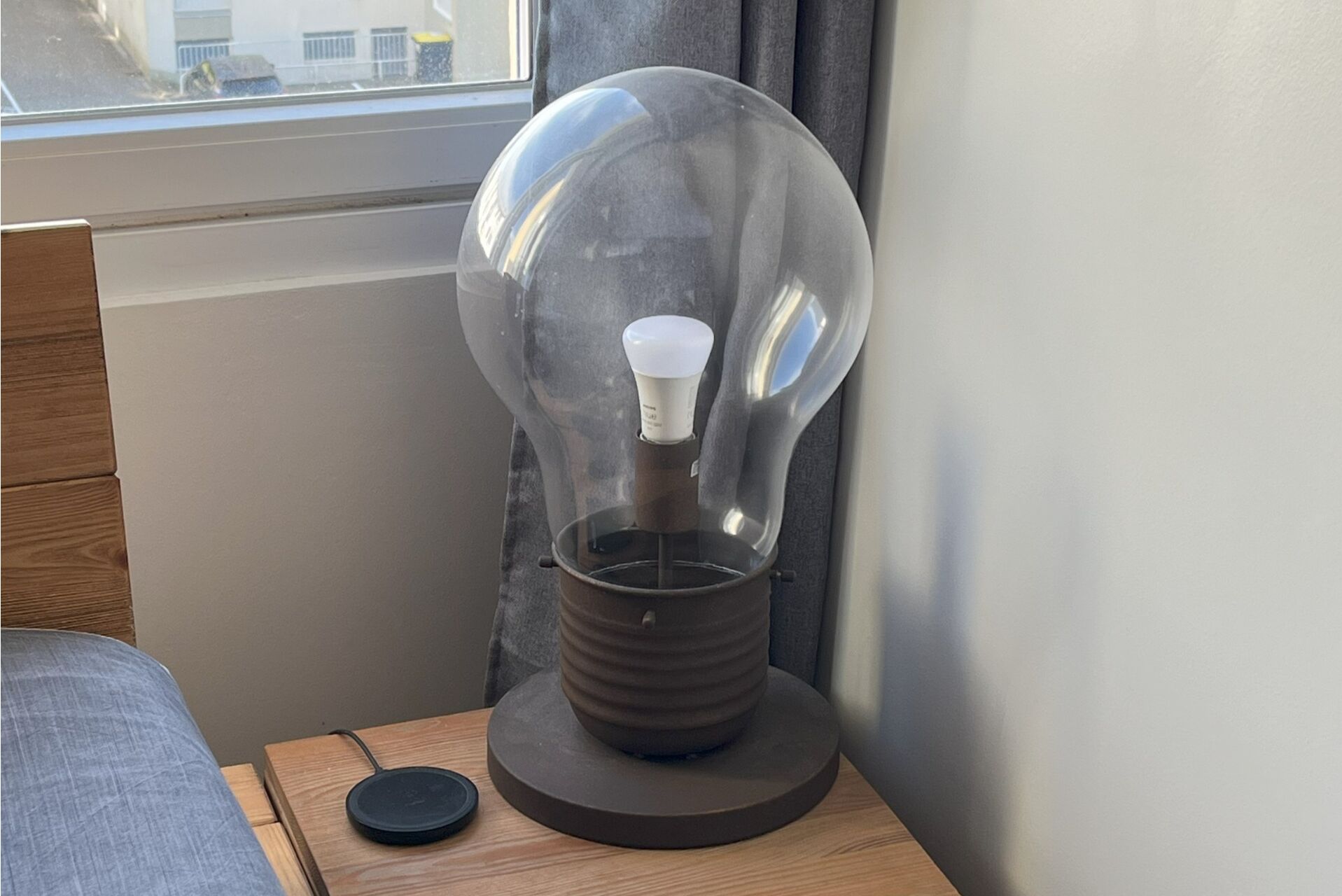 A lamp with a clear glass bulb and a white light bulb inside, placed on a wooden table next to a window.