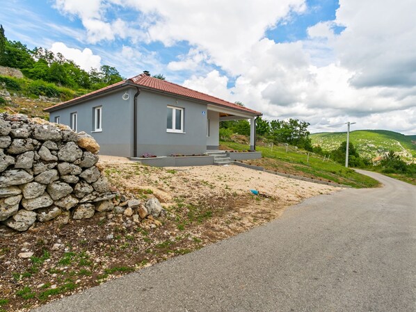 Une petite maison de plain-pied, avec un toit recouvert de tuiles rouges, située sur une colline et accessible par une allée en gravier.