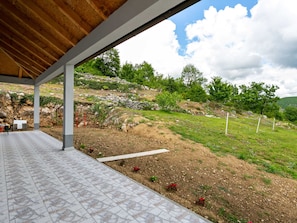 Relax in a serene outdoor space with a sheltered area overlooking a natural landscape of grassy terrain and rocky outcrops.
