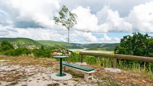 Banc i taula sobre un camí de grava amb vista a un riu i turons.