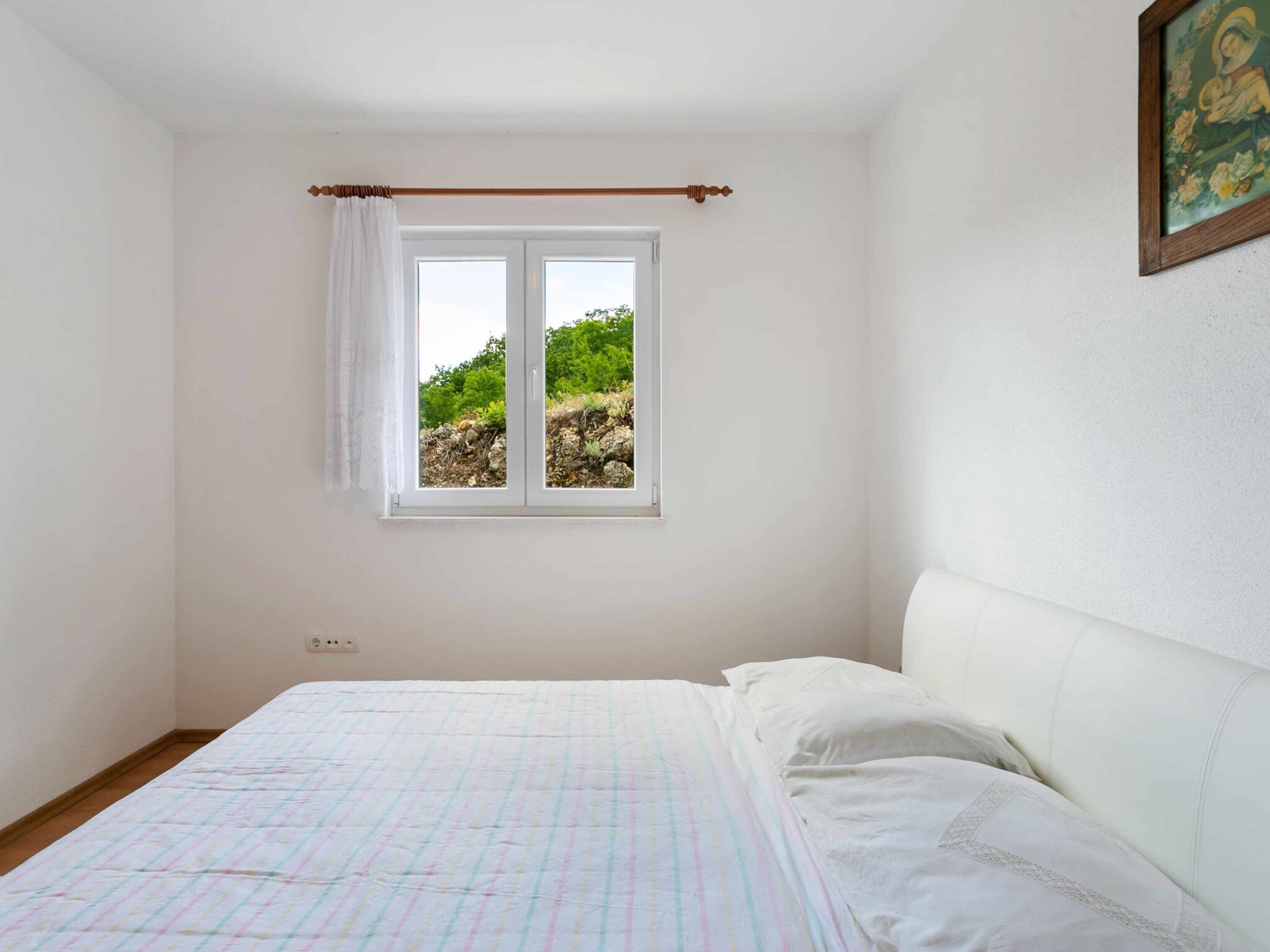 Une chambre à coucher avec un lit, une fenêtre donnant sur un paysage verdoyant et un tableau accroché au mur.