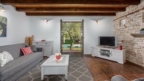 Un salon moderne avec un canapé gris, une table basse, un téléviseur posé sur un meuble blanc et un mur en pierre.