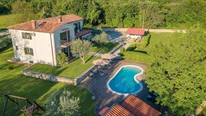 Une maison à deux étages avec une piscine, entourée d’une pelouse bien entretenue et d’arbres.