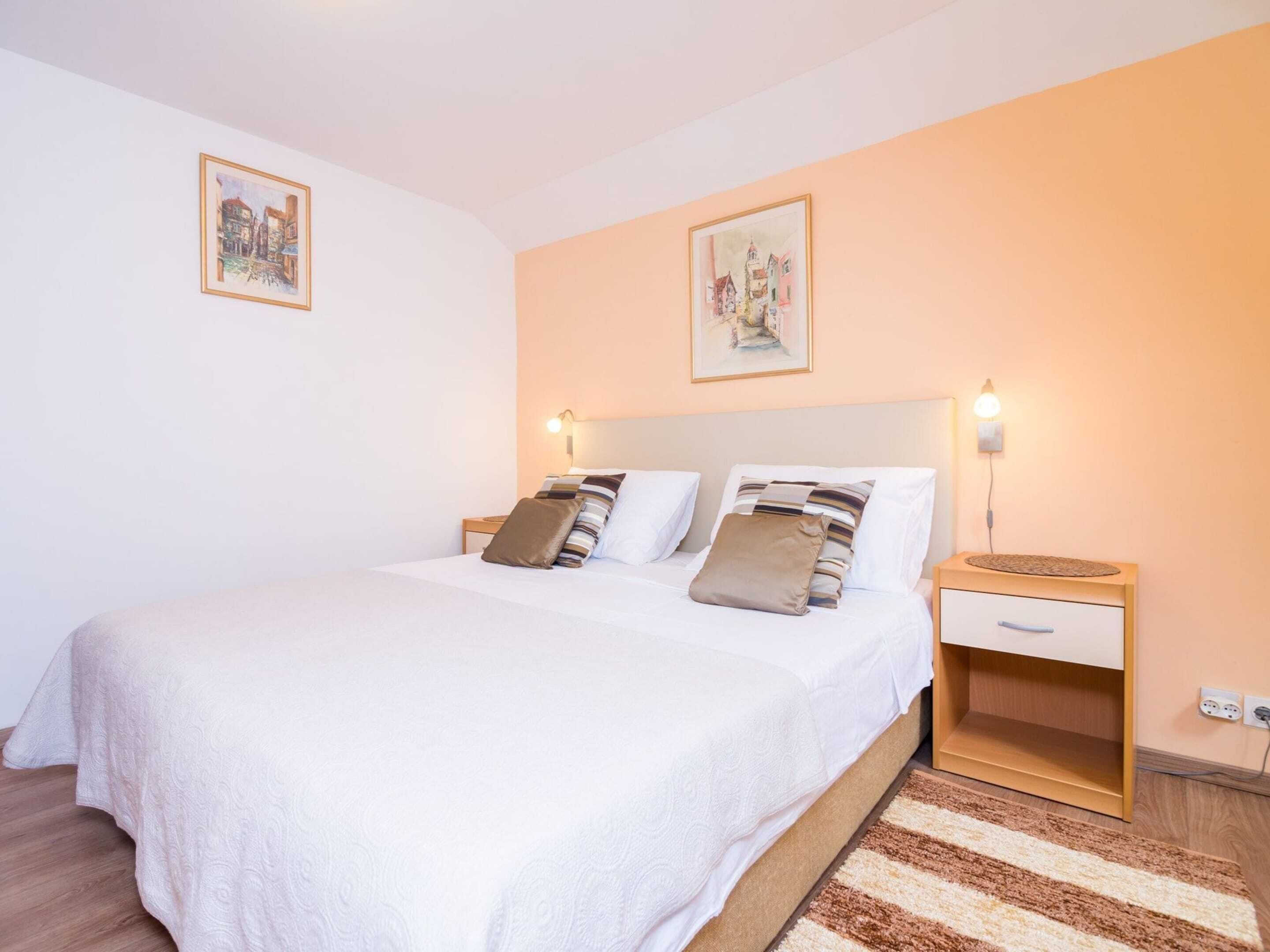 Une chambre à coucher avec un grand lit, deux tables de chevet, une table de chevet en bois avec une lampe, et deux tableaux encadrés accrochés au mur.