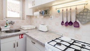 A kitchen with white cabinets, a gas stove, a sink, and various kitchen utensils hanging on the wall. - Apartment Neve - Two Bedroom Apartment (Dubrovnik)