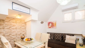 A modern living room with a glass dining table, a sofa, and a small side table with a bowl of fruit. - Apartment Neve - Two Bedroom Apartment (Dubrovnik)
