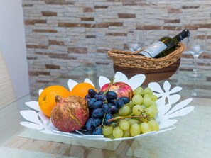Uma mesa de vidro com uma composição de frutas, uma garrafa de vinho e um copo.