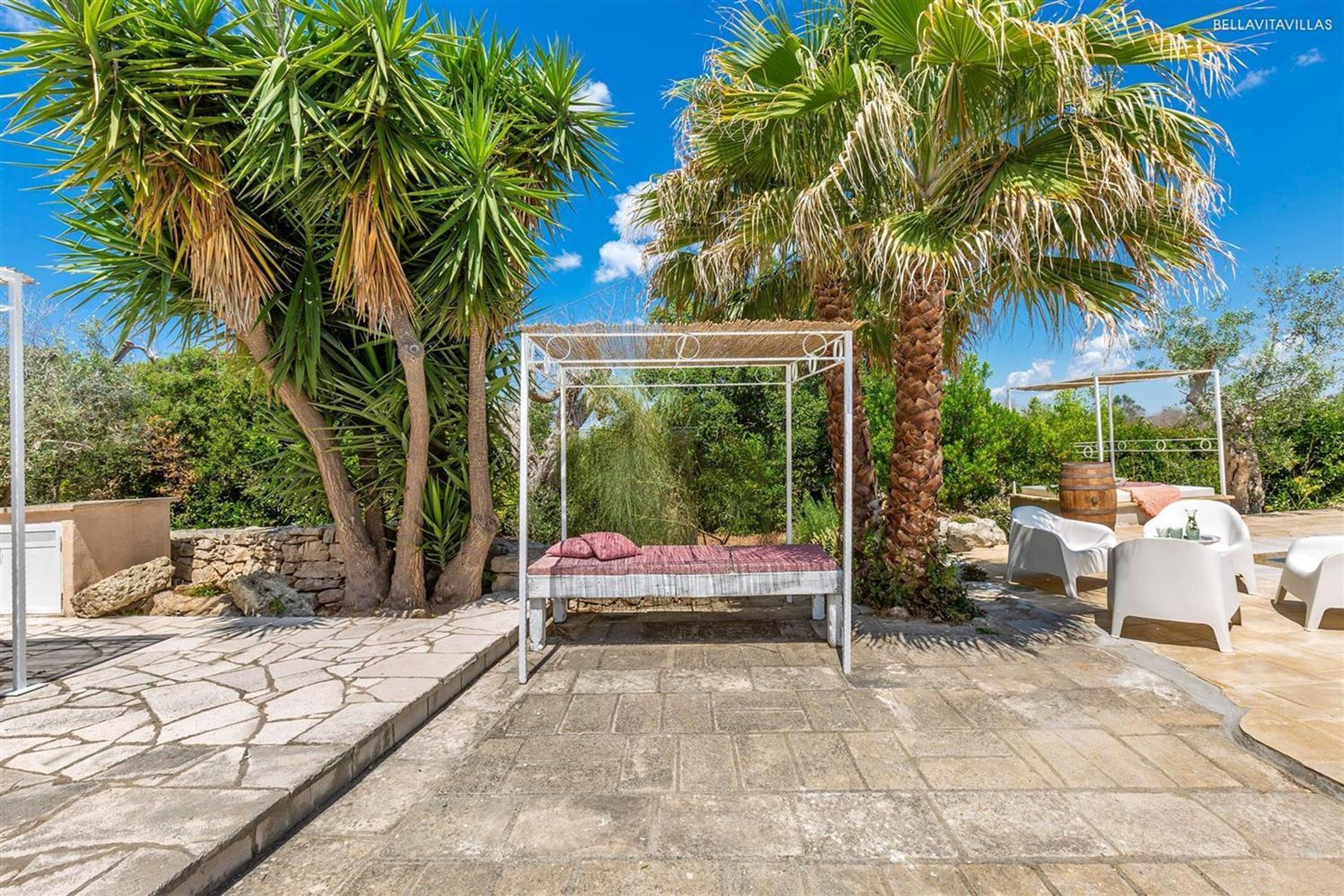 Un giardino con un'amaca, sedie bianche e un pergolato.