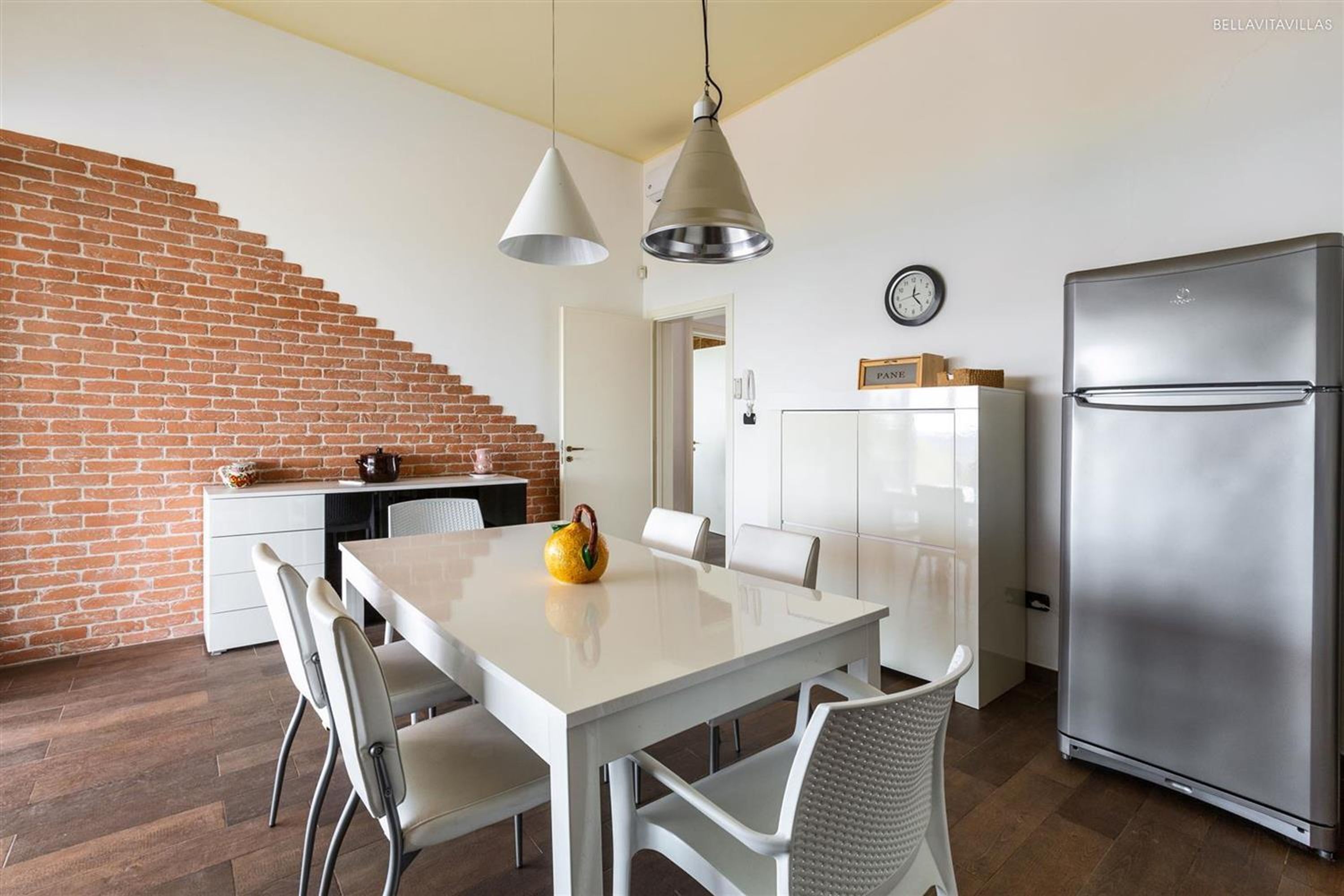 Una cucina moderna con una parete in mattoni, un frigorifero in acciaio inossidabile, un tavolo da pranzo con sedie e lampade a sospensione.