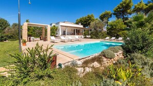 A poolside area with lounge chairs, a pergola, and a clear blue pool.