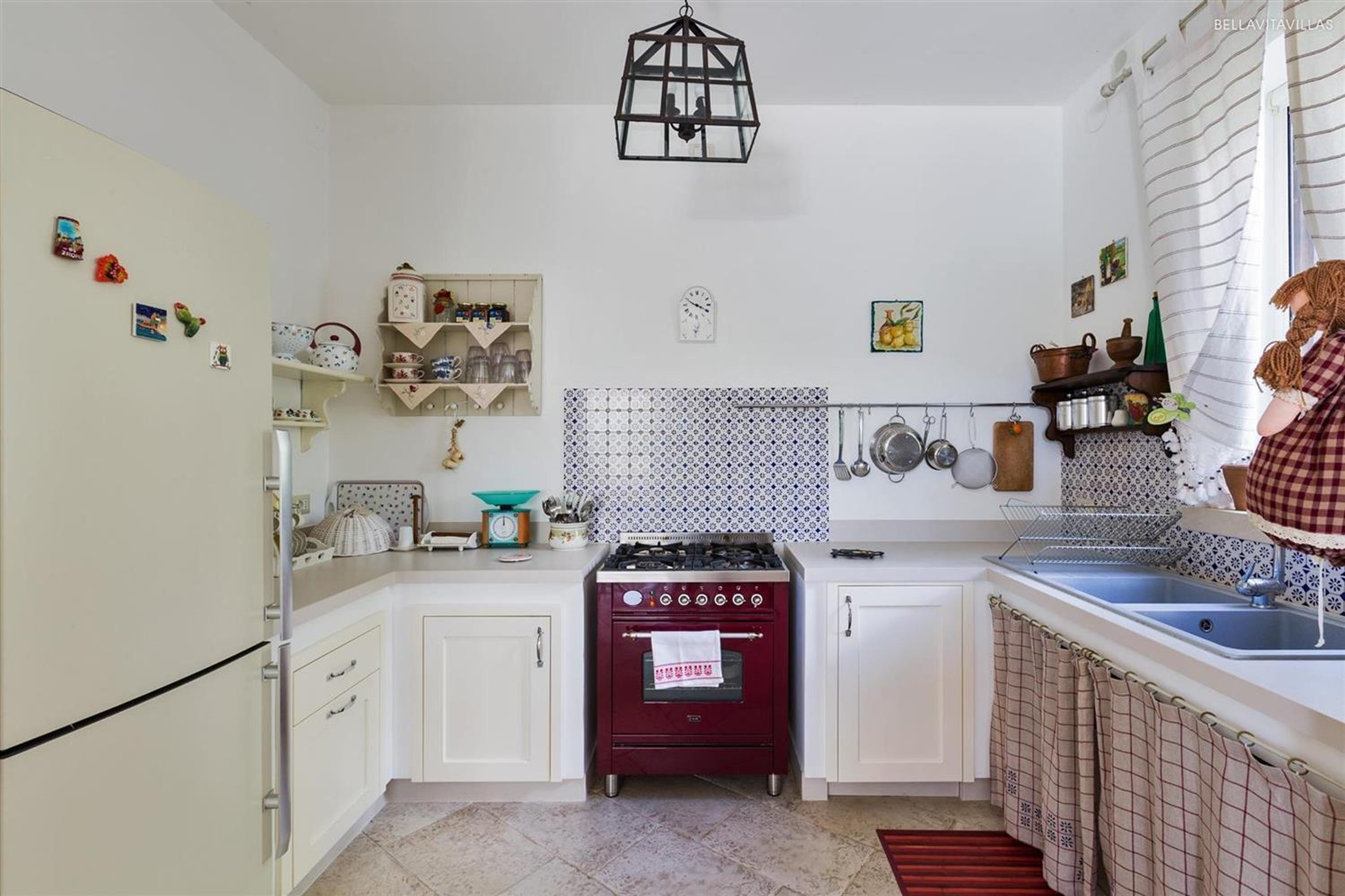 A compact kitchen with white cabinets, a red stove, and a hanging pot rack.