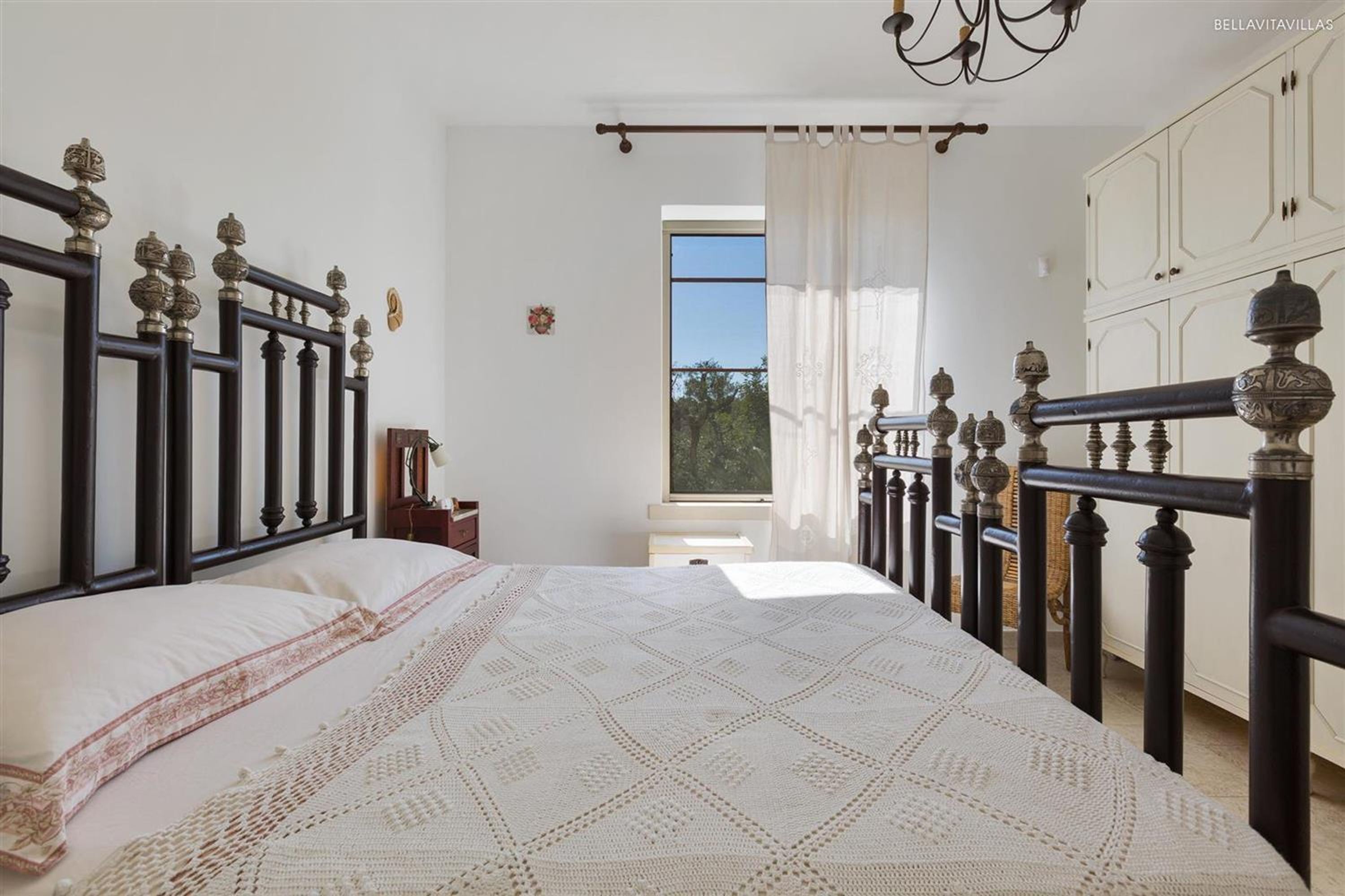 A bedroom with a large bed, a wooden headboard, a window with curtains, and a view of the outdoors.
