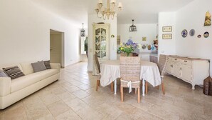 A dining area with a table and chairs, a chandelier, a sofa, and a cabinet.