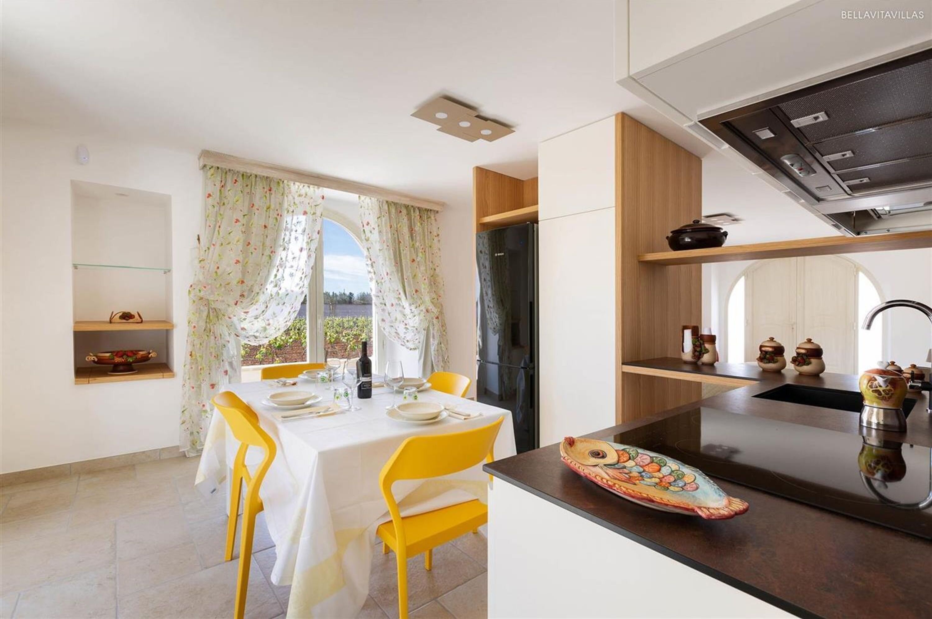 Una cocina moderna con un refrigerador negro, armarios de madera y un comedor con sillas amarillas y una mesa blanca.