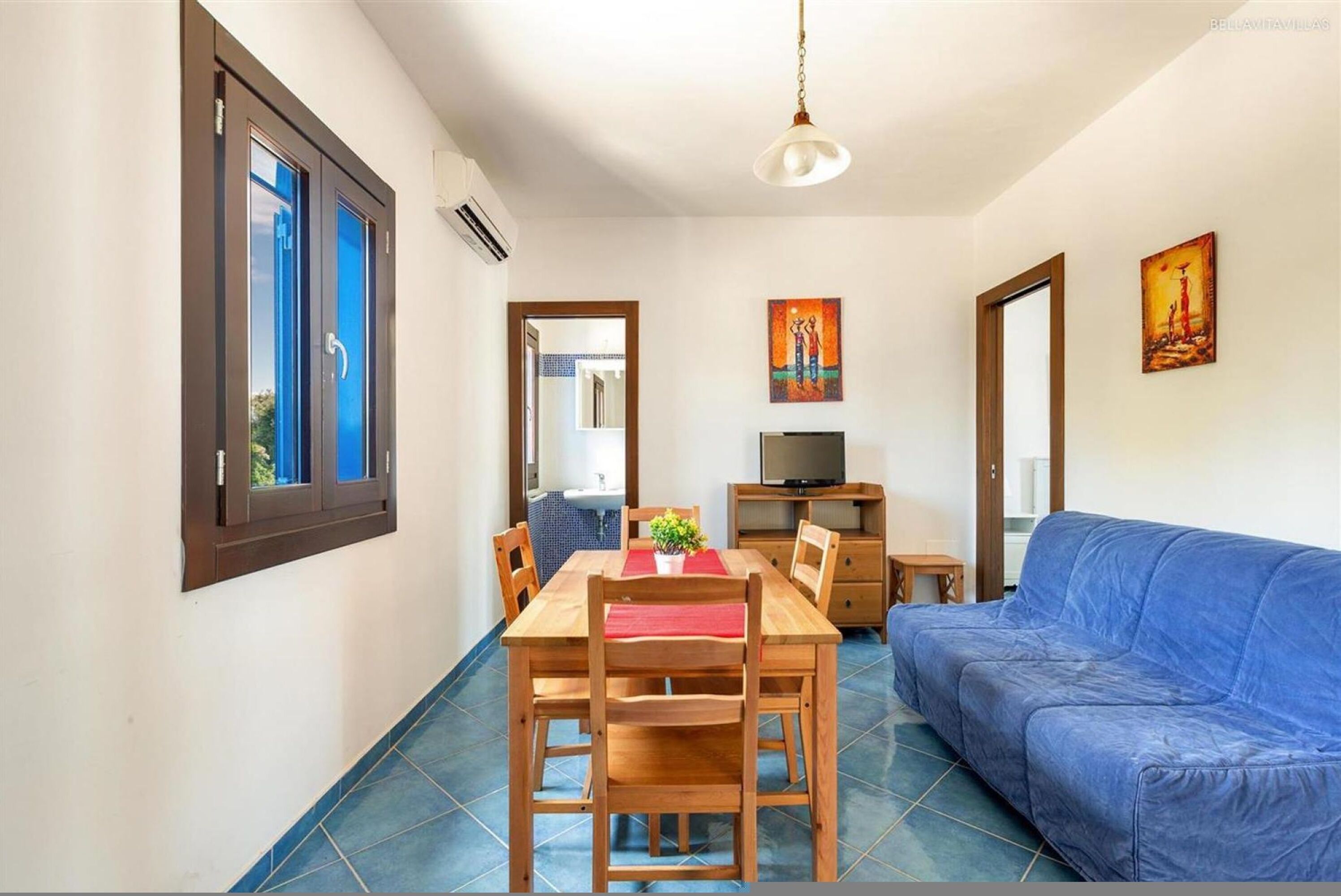 Ein Essbereich mit Holztisch und Stühlen, einem blauen Sofa und einem Fernseher auf einem Schrank.