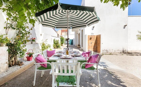 An outdoor dining area with a table set for four, surrounded by white chairs with green cushions. - 2068 Villa Marina Salentina (Porto Cesareo)
