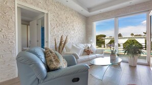 A modern living room with a stone wall, a blue sofa, a glass coffee table, and a view of greenery outside. - 2248 Villa Padangi in Gallipoli (Gallipoli)