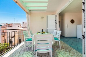 Ein Balkon mit Tisch für zwei Personen, Stühlen, einem Kühlschrank und Blick auf Gebäude.