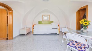Ein Schlafzimmer mit einem Bett, Nachttischen, einem Spiegel, einem kleinen Tisch mit Blumen und einem Sessel.