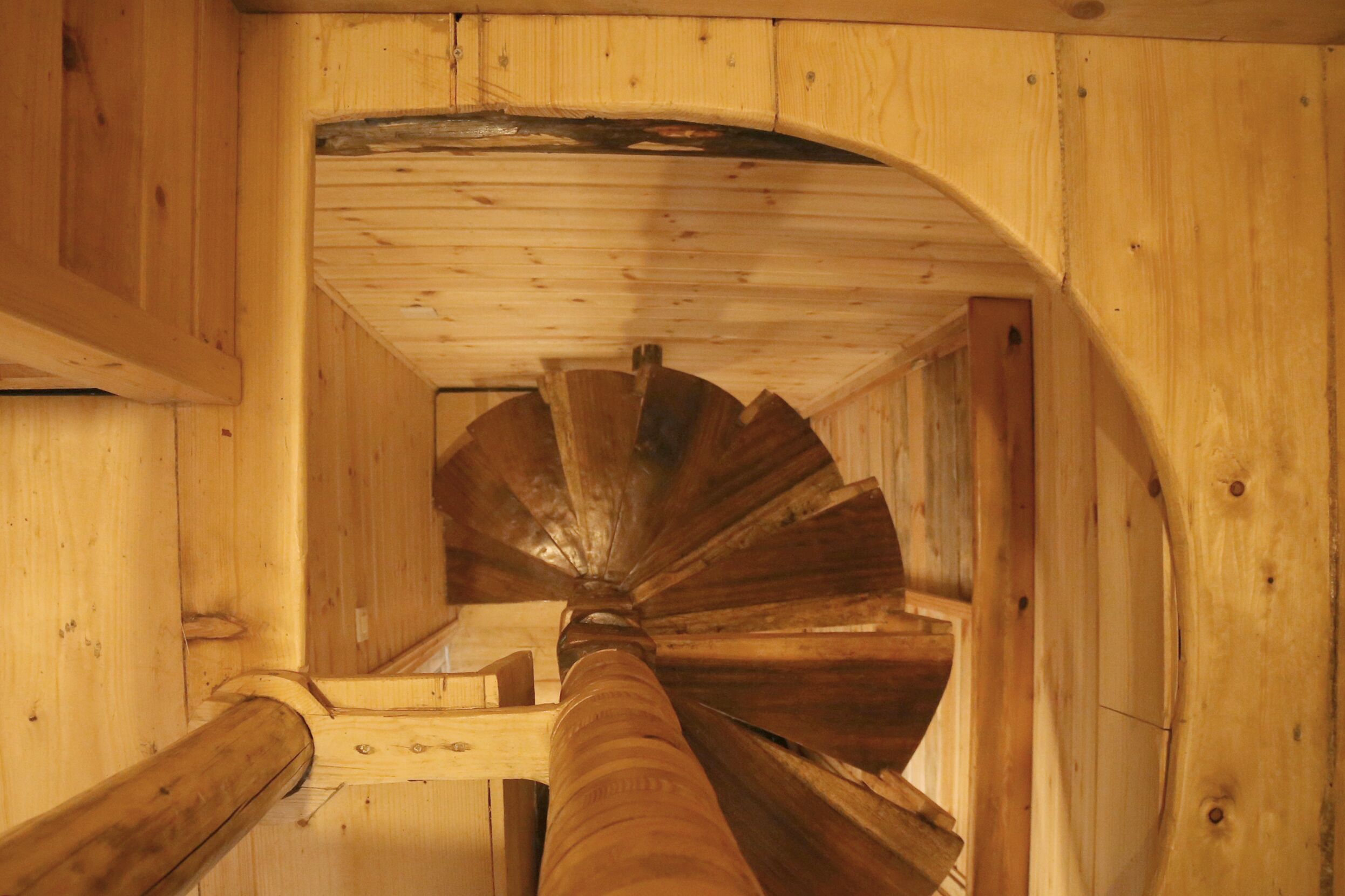 A wooden spiral staircase with a handrail, leading to an upper floor.