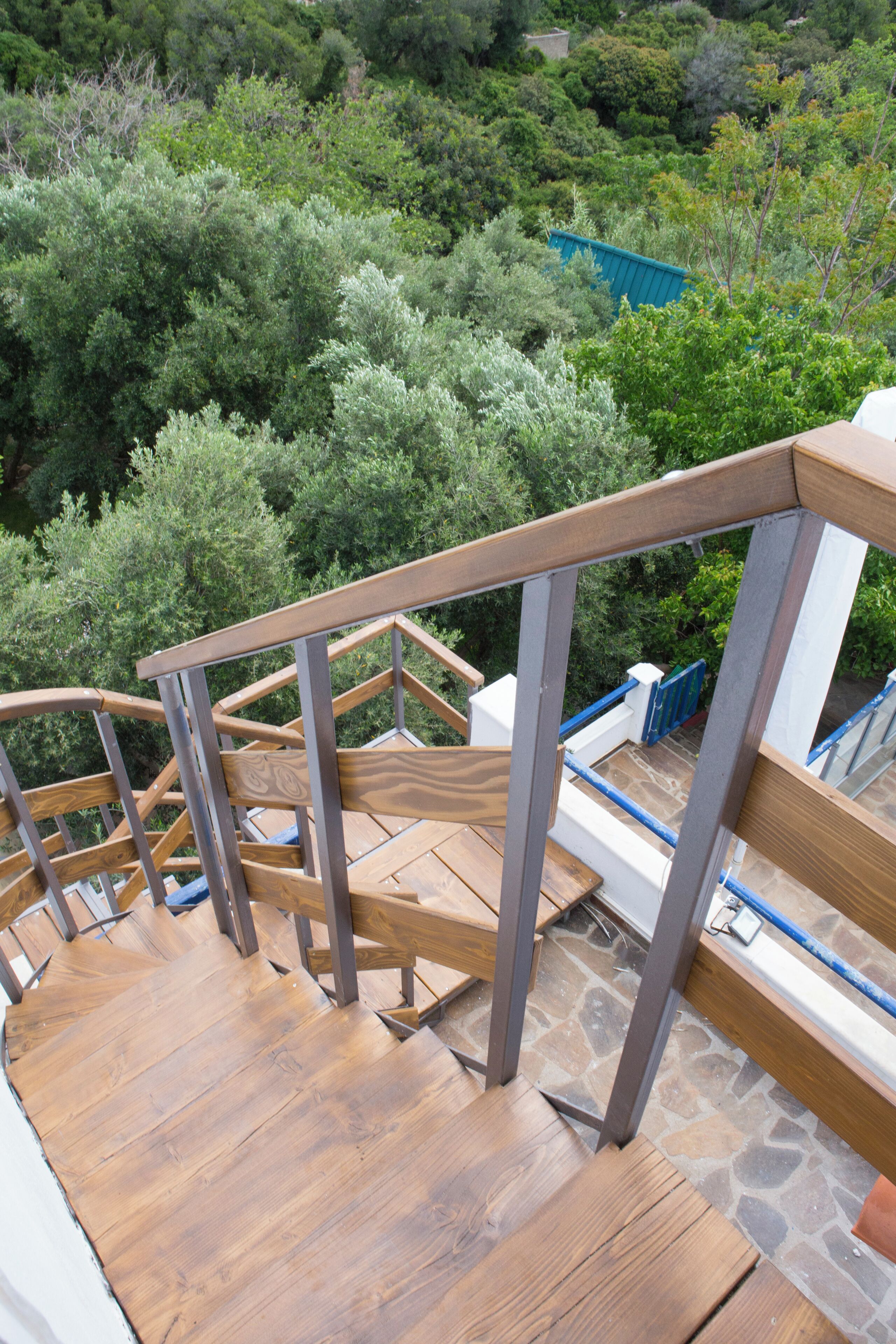 A wooden staircase with metal railings leading to a stone floor.