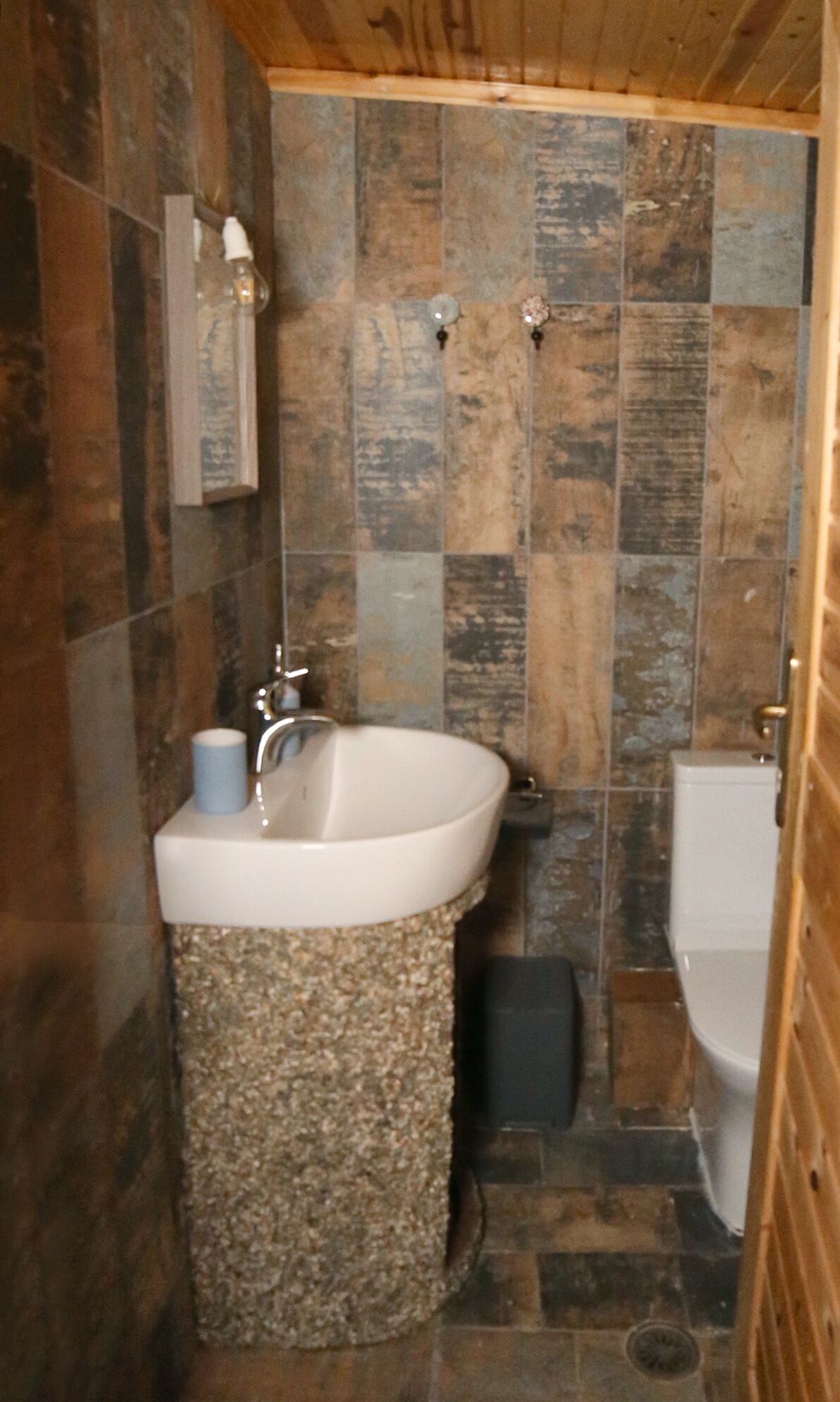 Un baño con pared de piedra, un lavabo con toalla y un inodoro.