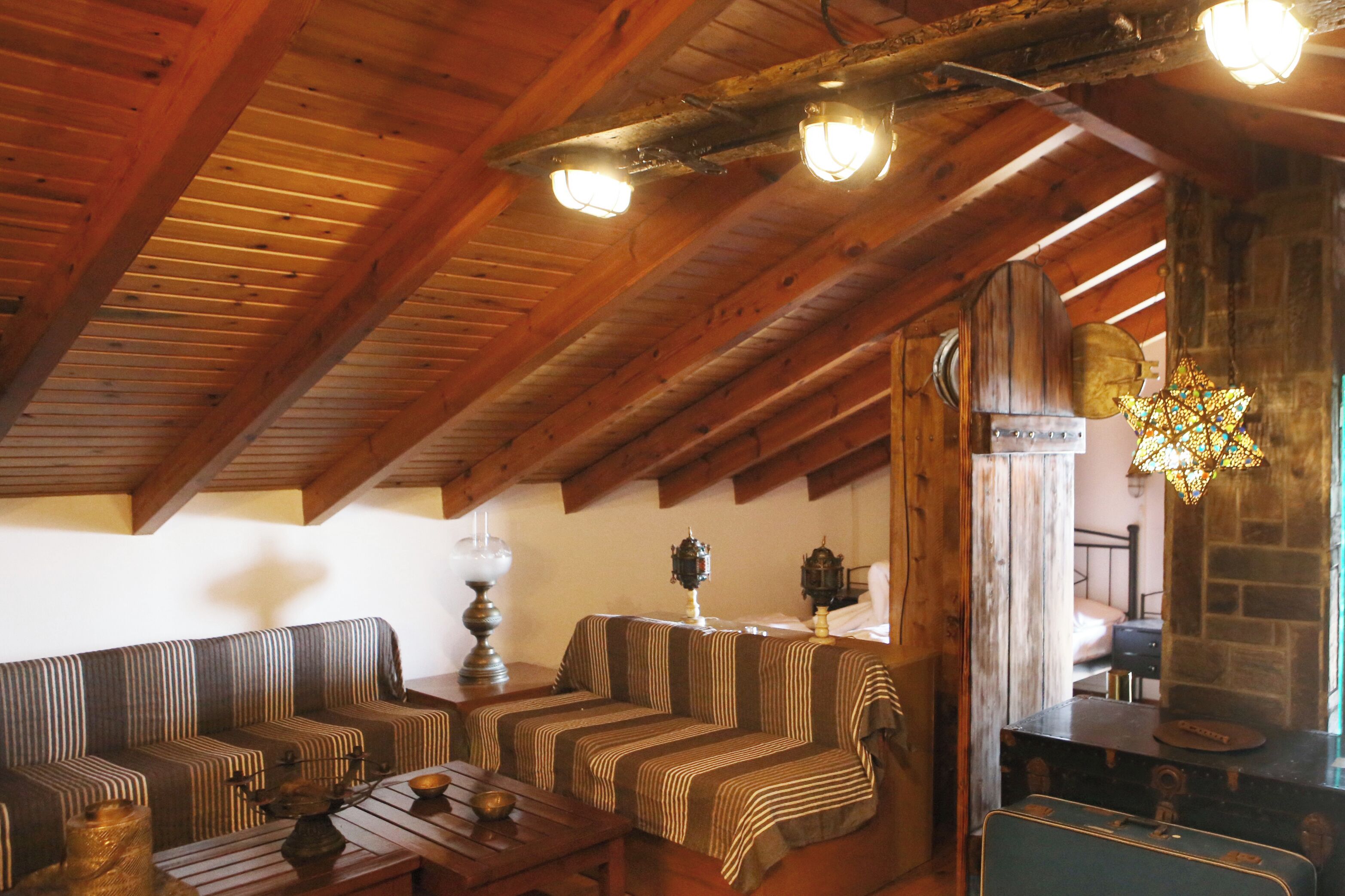 Un acogedor dormitorio en ático con vigas de madera, un conjunto de sofá a rayas, una mesa con lámpara, y un aplique decorativo con forma de estrella.