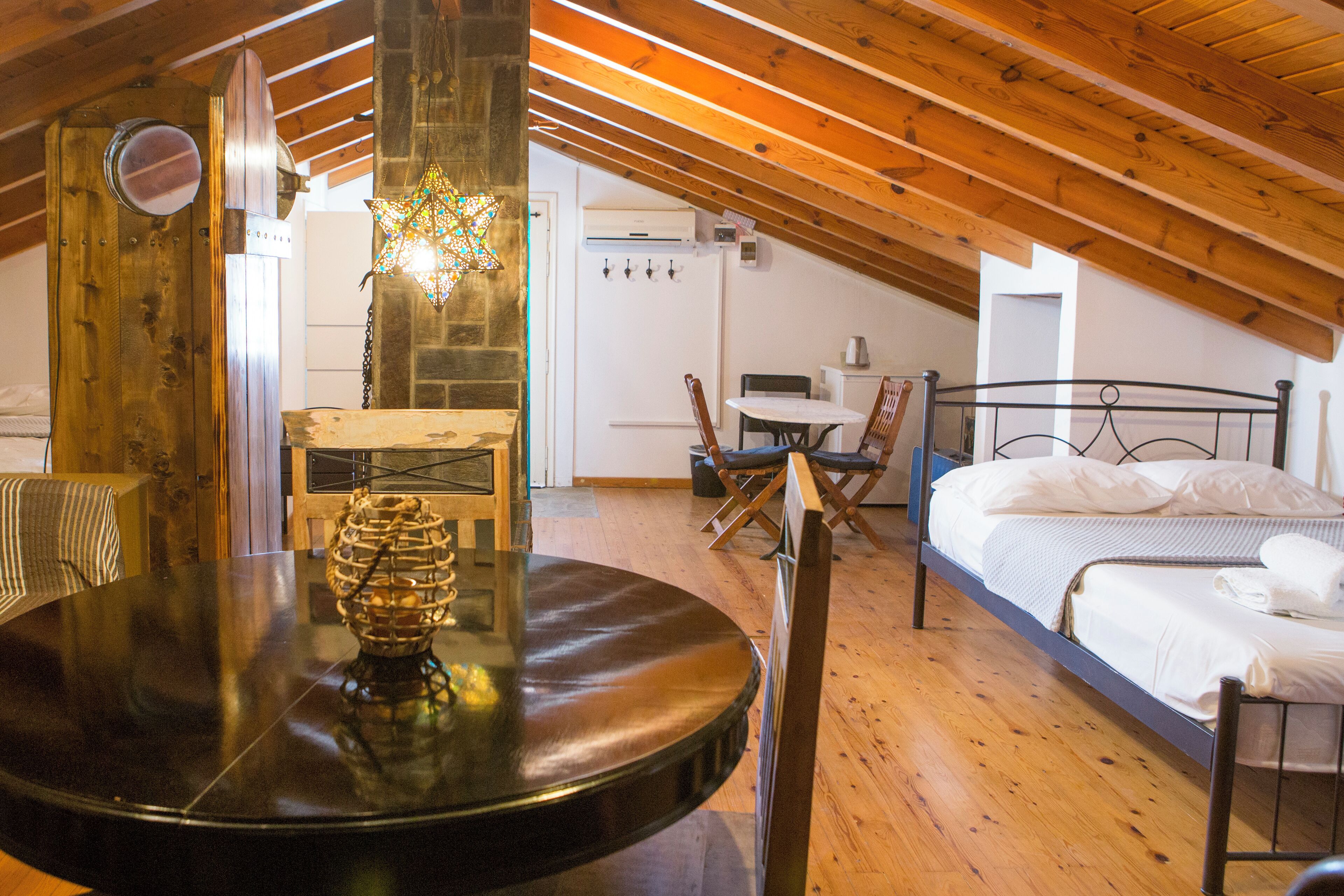 Un dormitorio acogedor en el ático con techo de madera, una mesa redonda con un centro decorativo, una cama con ropa blanca y una pequeña zona de comedor.
