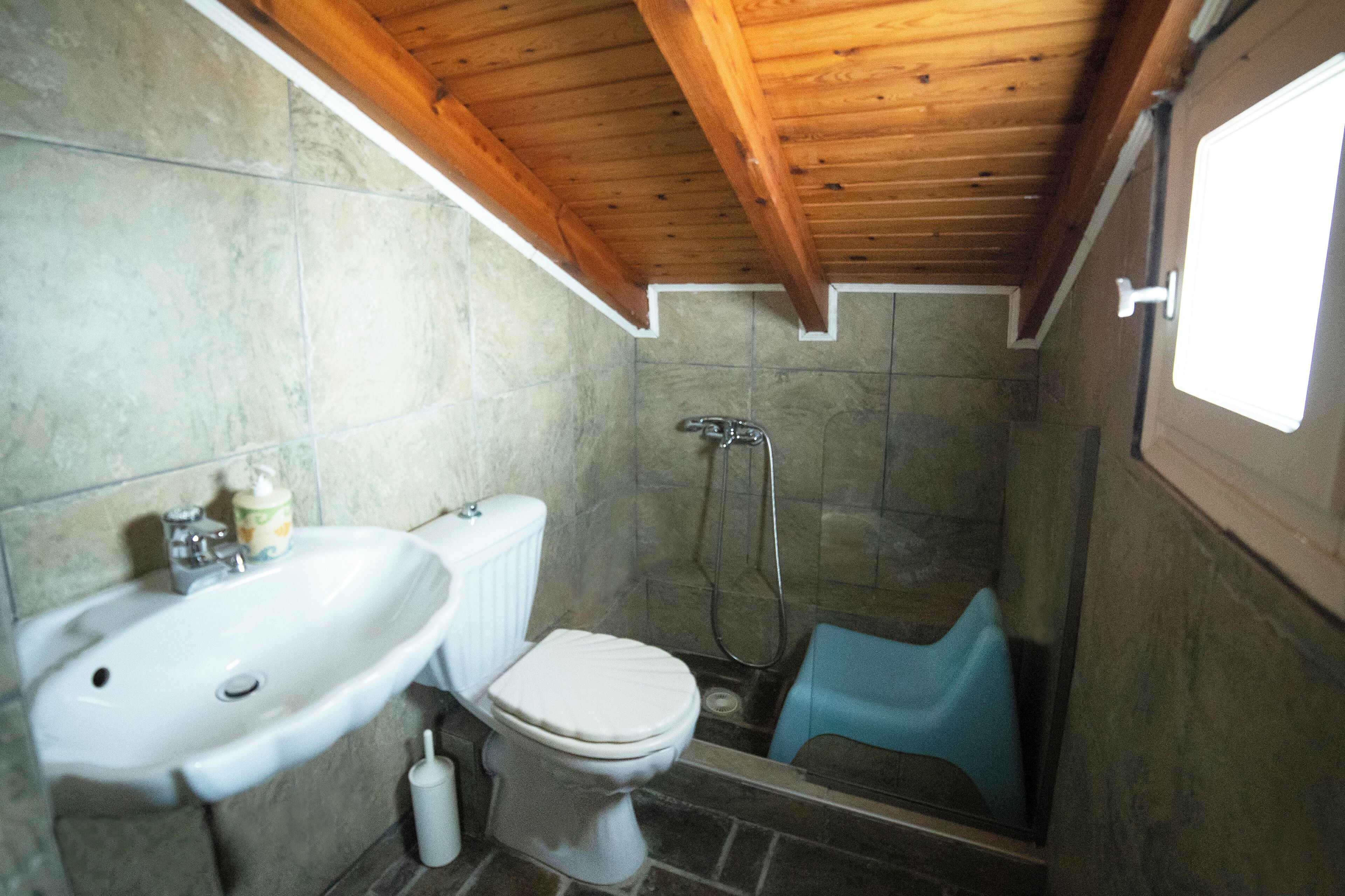 A bathroom with a wooden ceiling, a white sink, a toilet, and a shower area.