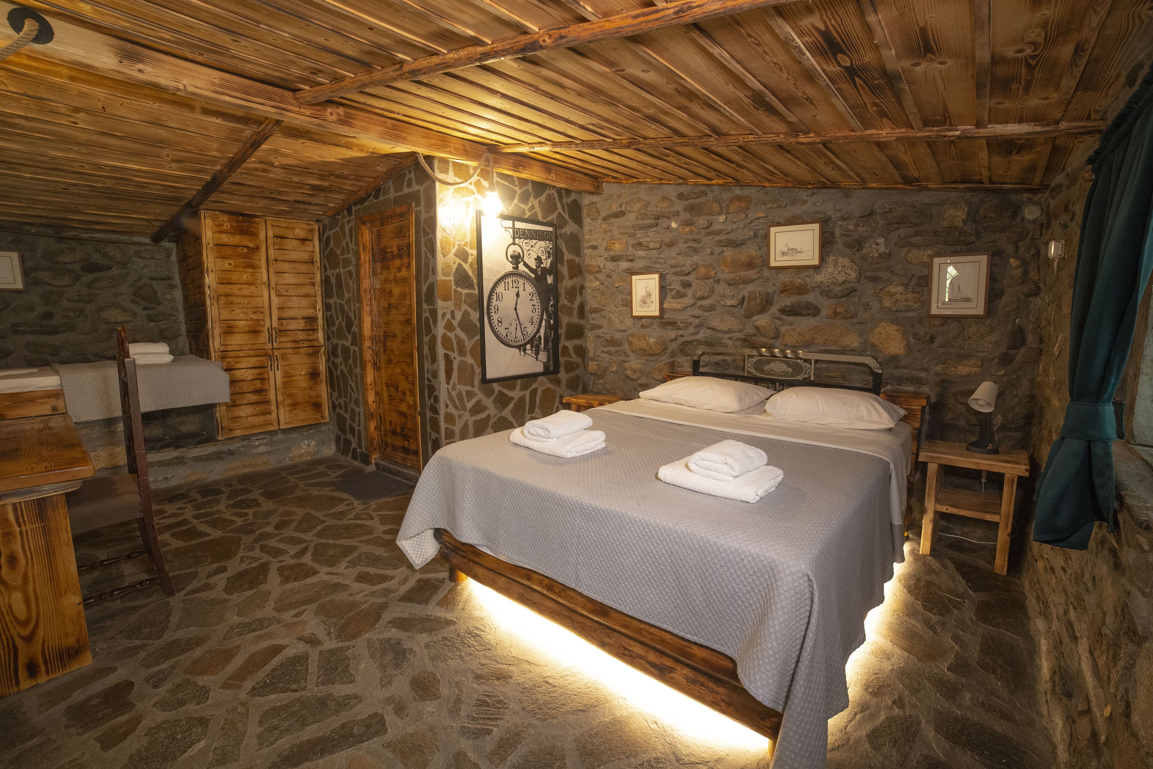 A rustic bedroom with a stone wall, wooden ceiling, and a bed with neatly folded towels.