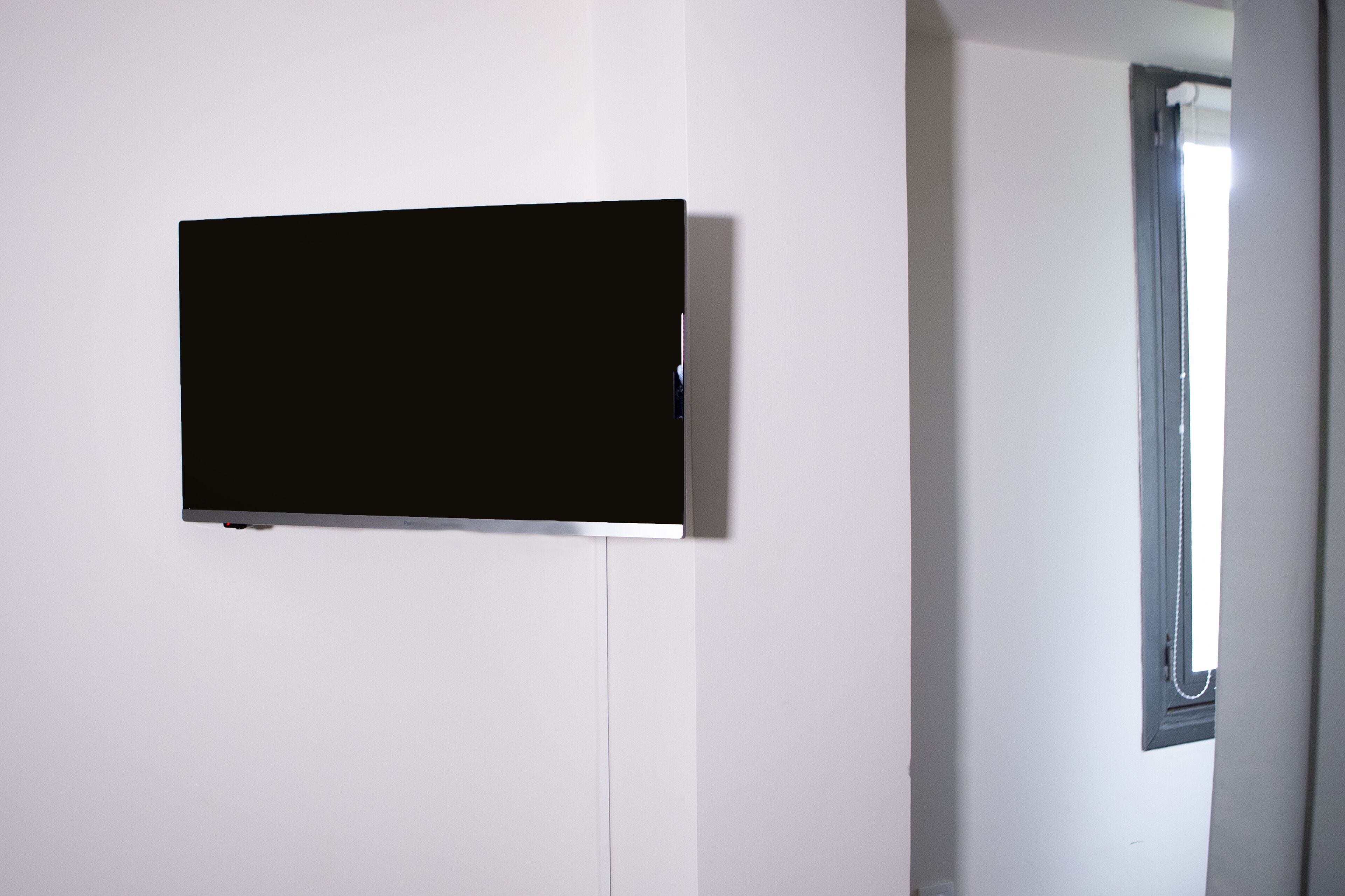 Un televisor de pantalla plana montado en una pared blanca en una habitación con una puerta y una ventana.