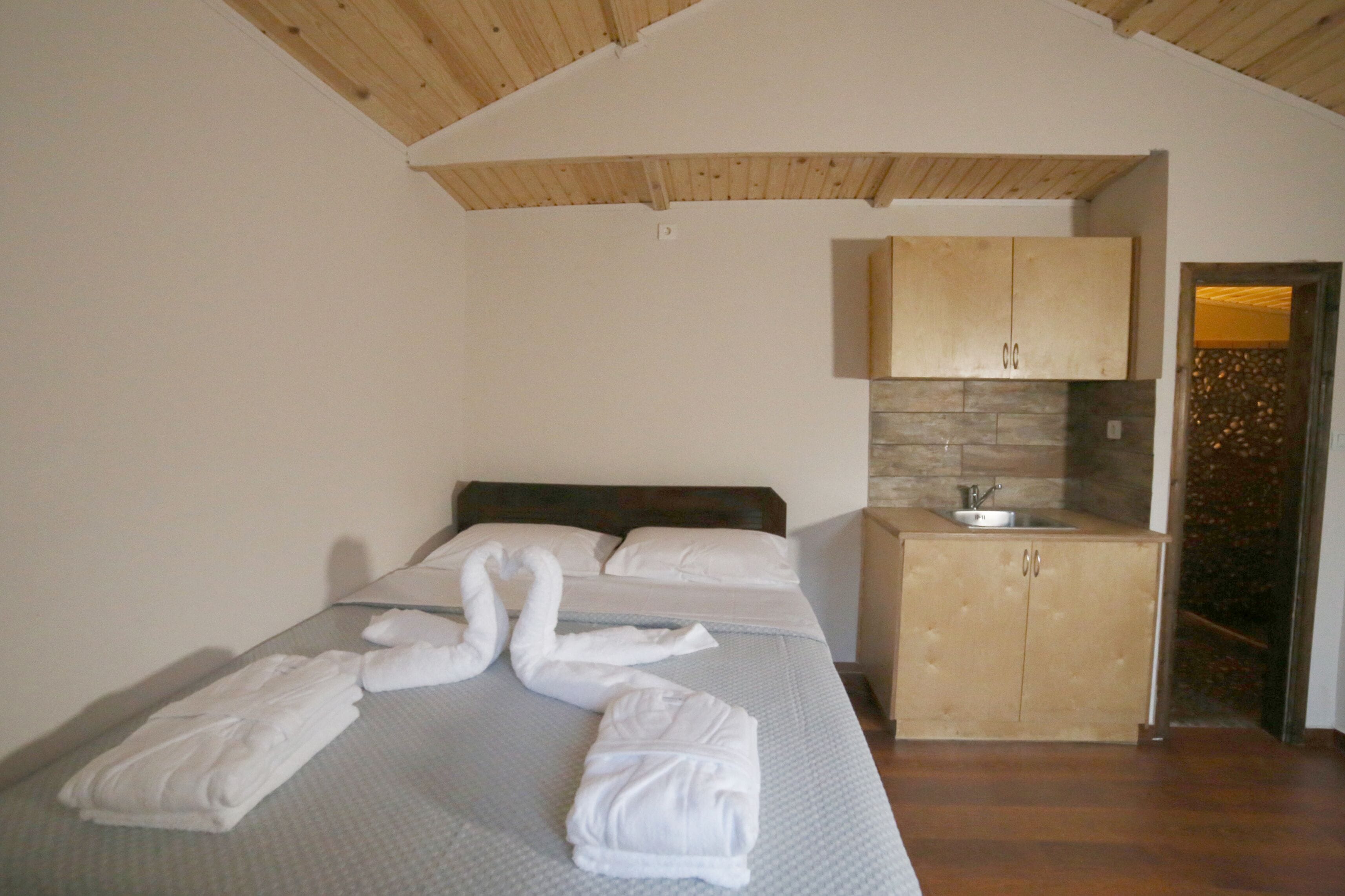 Ein Schlafzimmer mit einem Bett, einem Holfachschrank mit Waschbecken und einer zu einem Schwan geformten Handtuch.'