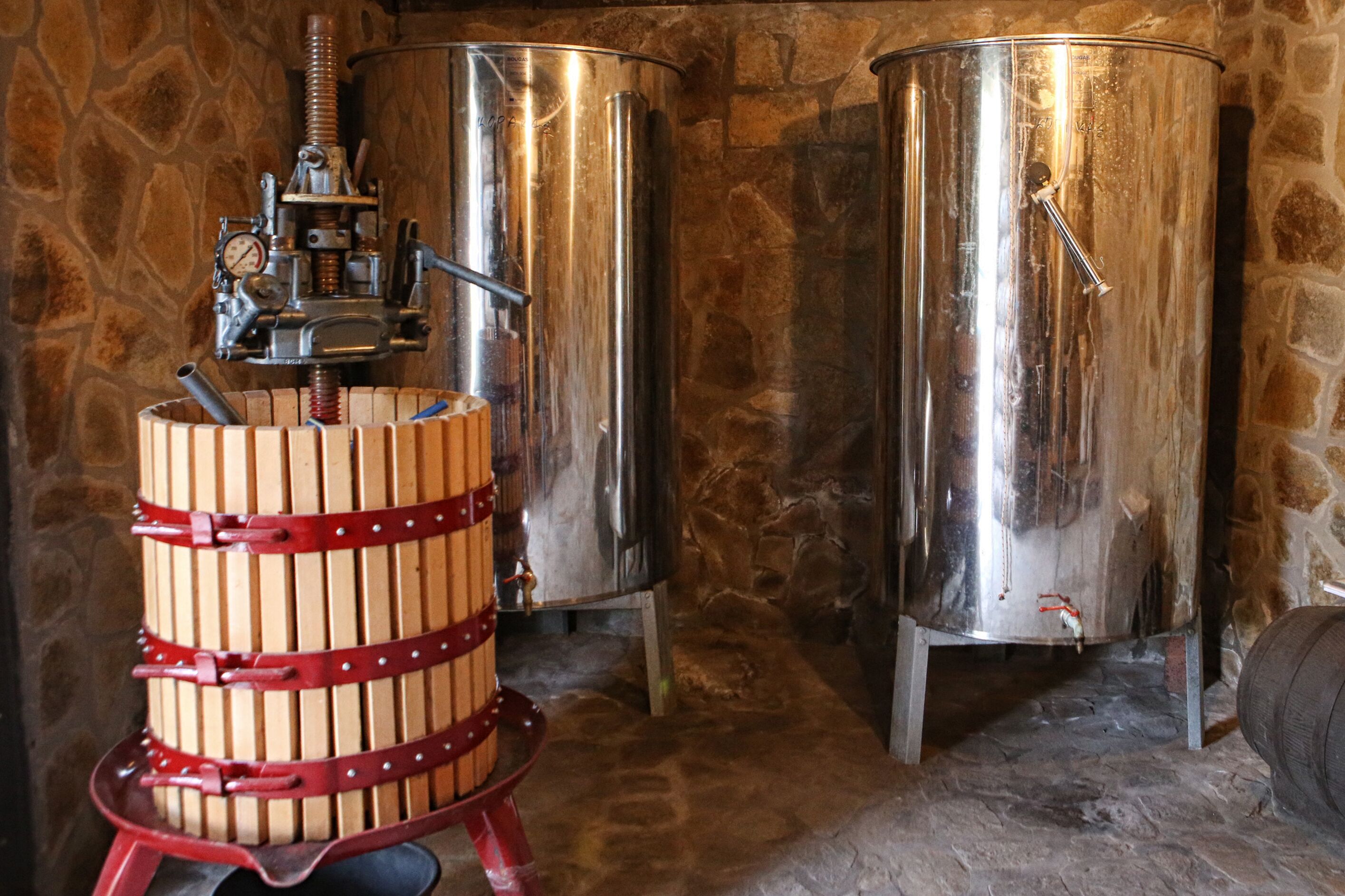 Two stainless steel tanks and a wooden barrel with a pump in a stone-walled room.