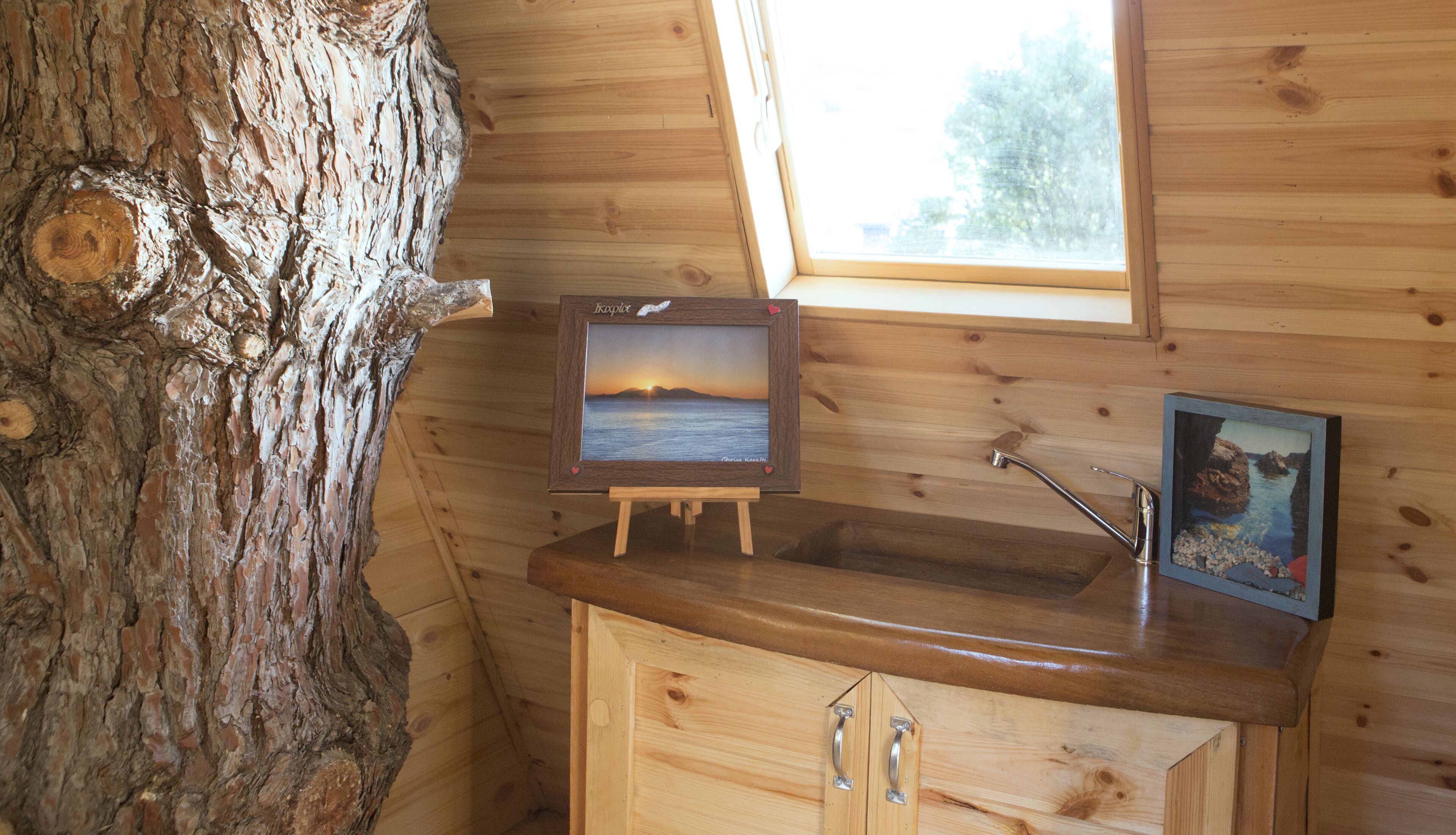 Interior de una cabaña de madera con un armario de madera, un caballete con un cuadro enmarcado y una ventana con vistas al exterior.