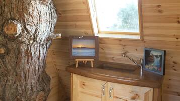 Interior de una cabaña de madera con un armario de madera, un caballete con un cuadro enmarcado y una ventana con vistas al exterior.