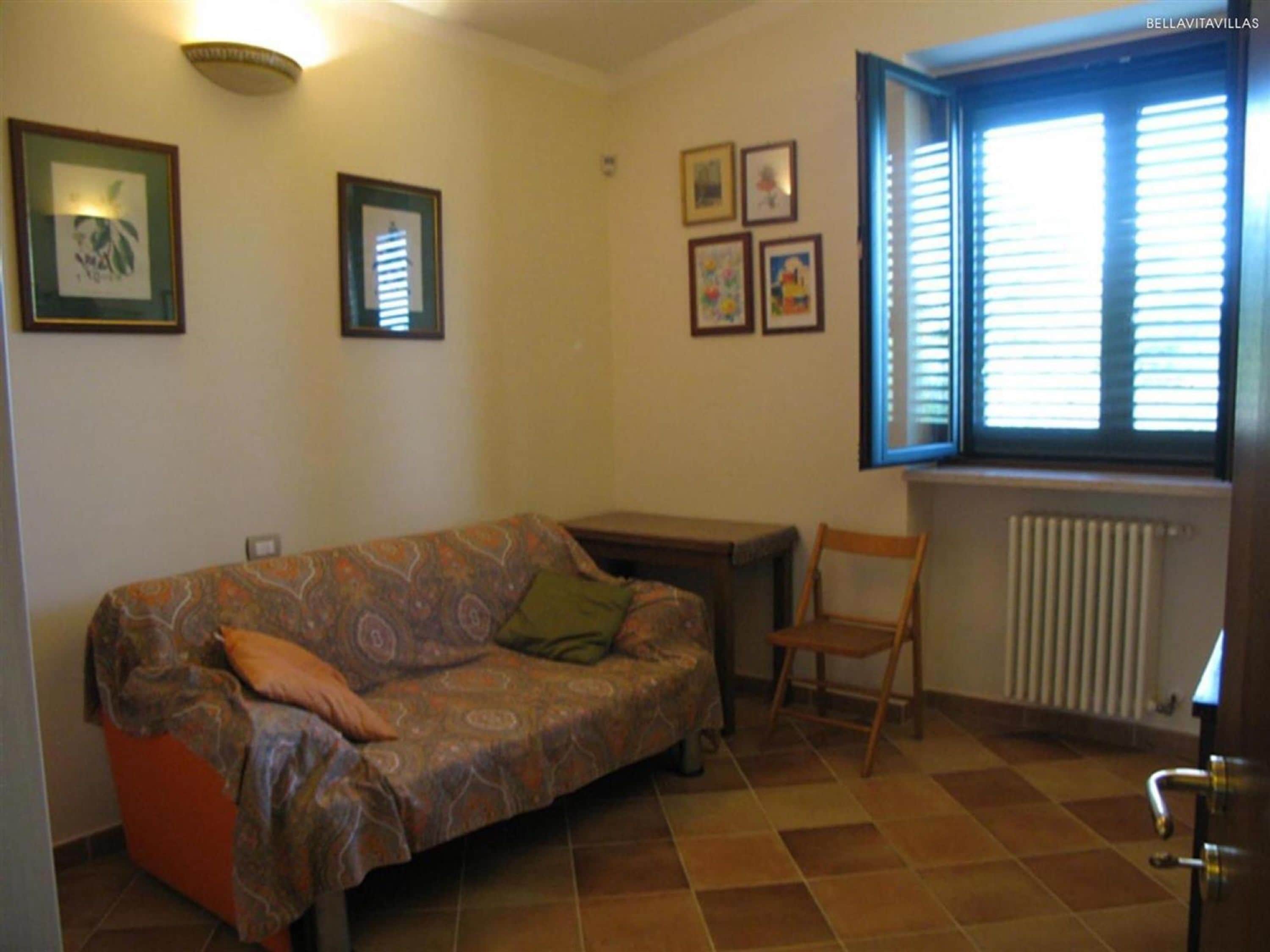 A living room with a patterned sofa, a small table, a chair, and a window with blinds.