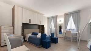 A modern hotel room with a bed, a desk, and a chair. There is a wardrobe and a small seating area with ottomans. - 1283 B B Dreams and Delights - Sea Sight Camera Familiare (Porto Cesareo)