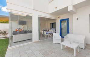 A modern outdoor patio area with a glass door leading to a dining space, white wicker furniture, and a blue door. - 1283 B B Dreams and Delights - Sea Sight Camera Familiare (Porto Cesareo)