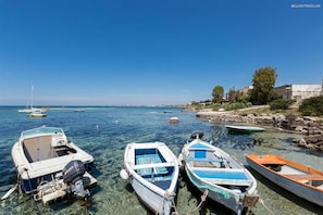 A coastal scene with several boats tied to the shore, clear water, and a distant view of the sea.