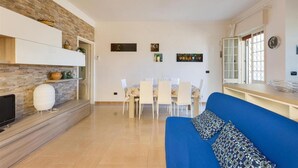 A modern living room with a blue sofa, a dining area with white chairs, and a kitchen with stone backsplash and white cabinets.