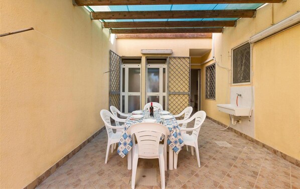Une petite terrasse avec une table et des chaises, une fenêtre ornée d’une grille en métal et un évier fixé au mur.