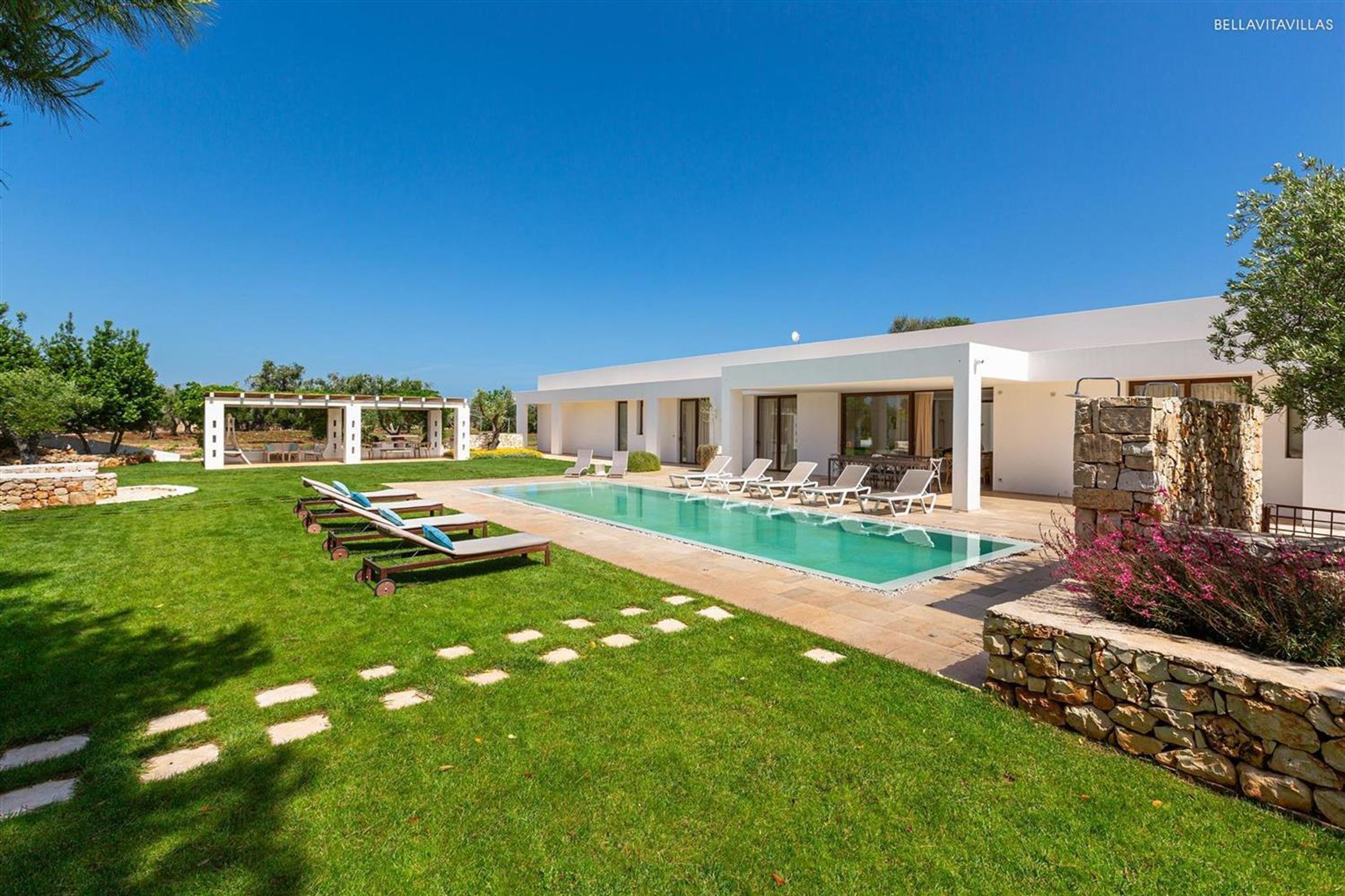 A modern villa with a swimming pool, lounge chairs, and a stone wall.