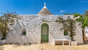 Um edifício branco com porta verde, duas janelas pequenas e telhado de pedra.