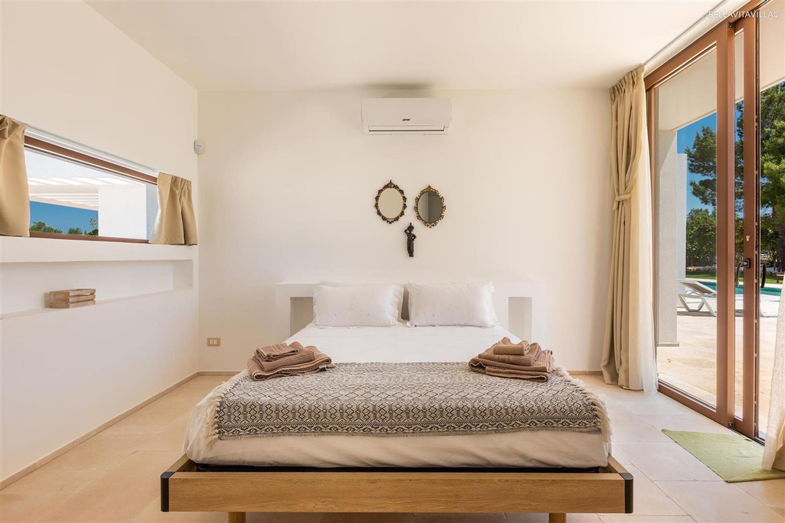 Une chambre à coucher avec un lit, une fenêtre, un climatiseur fixé au mur et une vue sur l’extérieur.