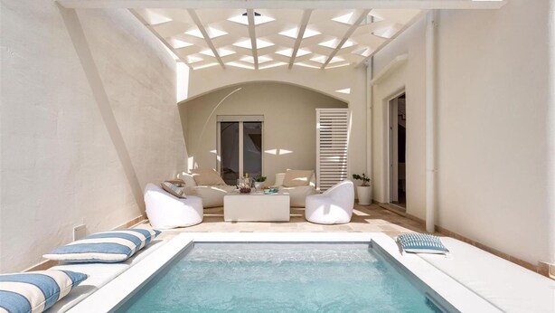 Zona de piscina amb un sostre il·luminat pel sol, gandules blanques i una taula petita amb objectes decoratius.